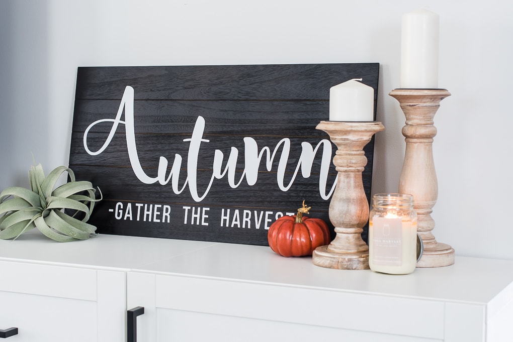 black and white wooden autumn sign with an orange pumpkin and natural wood candle holders