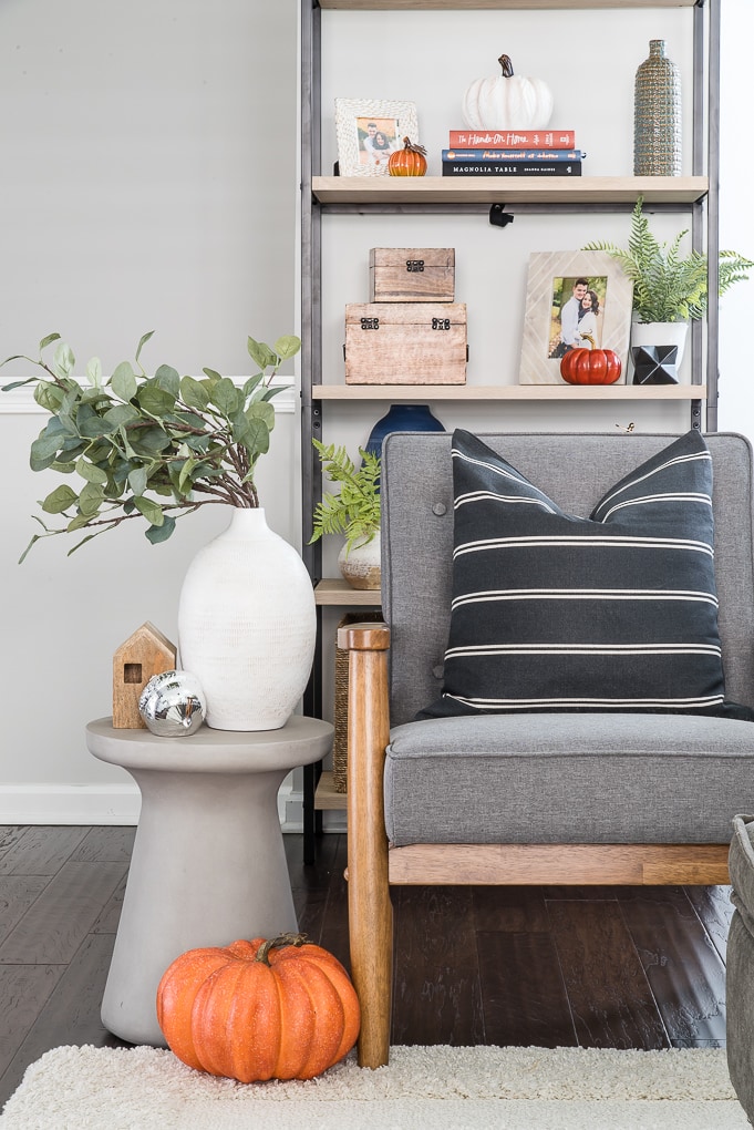 accent chair and side table with a white vase and eucalyptus and orange pumpkin