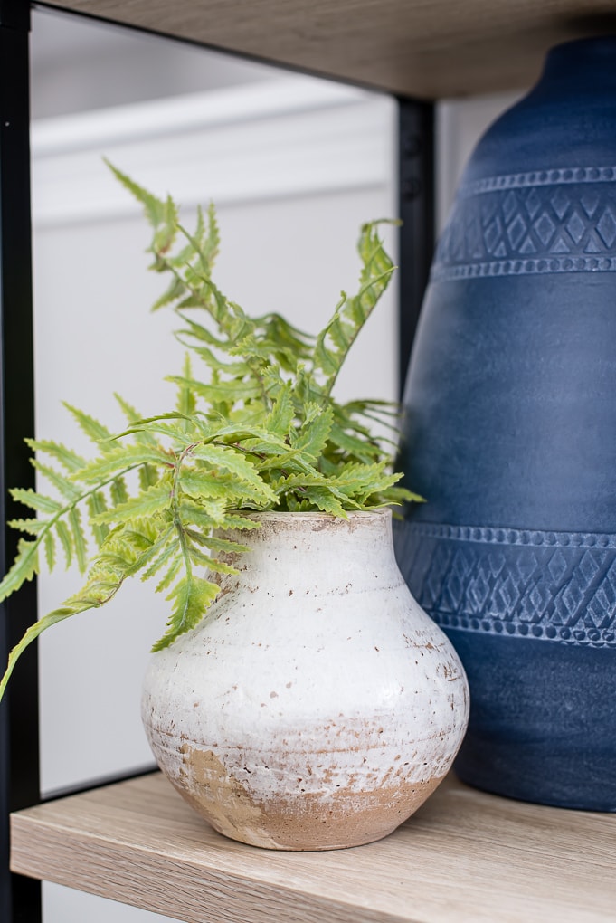 green faux floral stem in a natural clay vase on a bookshelf