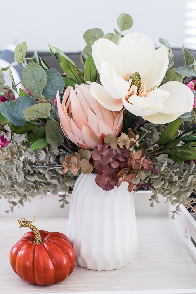 fall floral arrangement in a white vase with an orange pumpkin