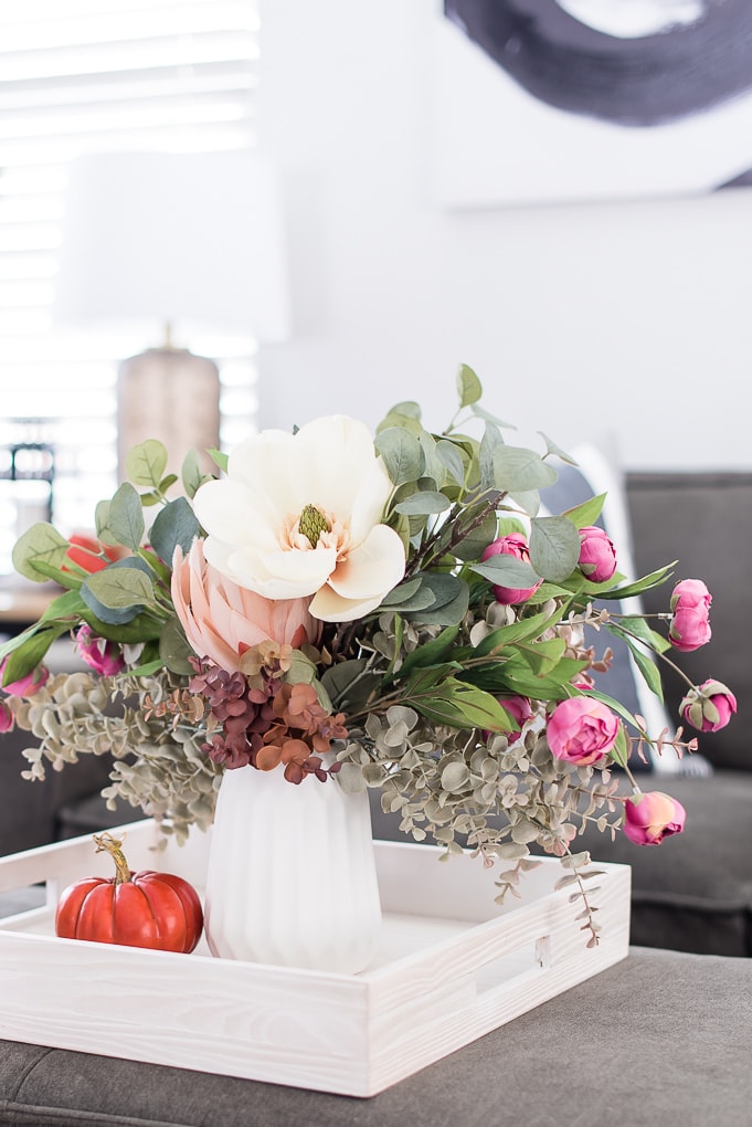 fall floral arrangement in a white vase on a tray with an orange pumpkin