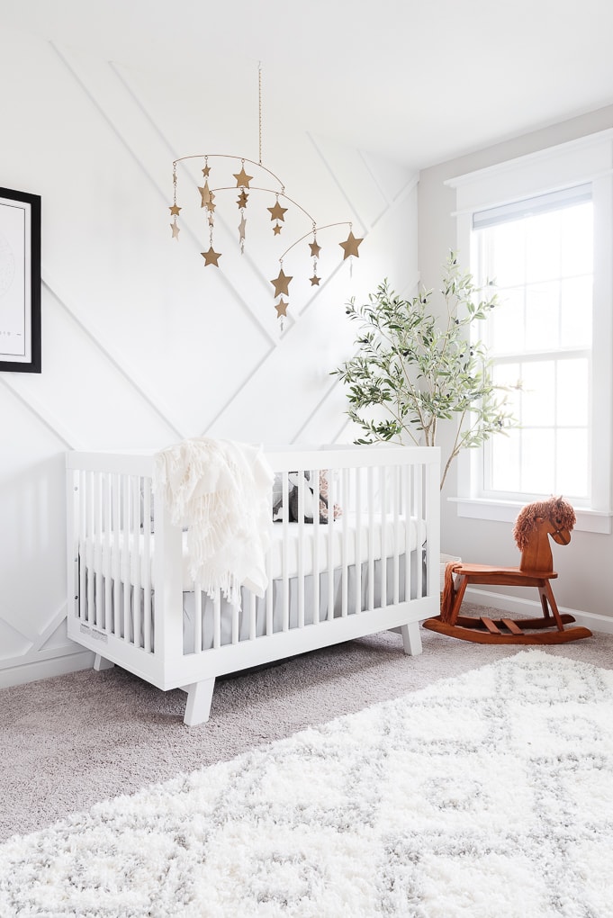 modern neutral feminine nursery with a white crib and a white accent wall