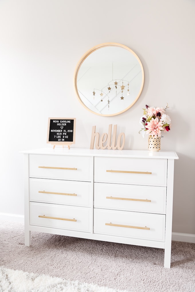 white dresser with a gold circle mirror and decorative accents on the top in a nursery