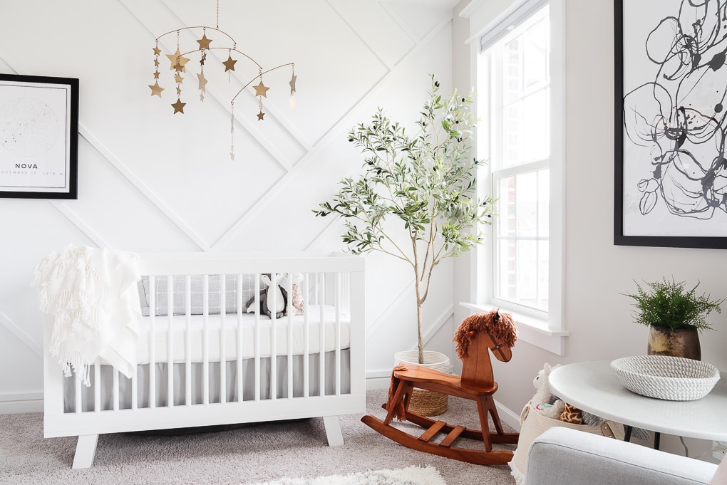 white crib and wooden rocking horse in front of a white modern accent wall in a nursery