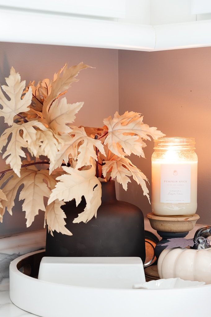 black vase with fall leaves and antique candle co candle burning in kitchen