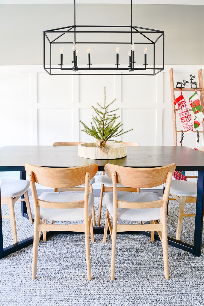 sparse tabletop Christmas tree in natural round wooden tray on top of modern black dining room table