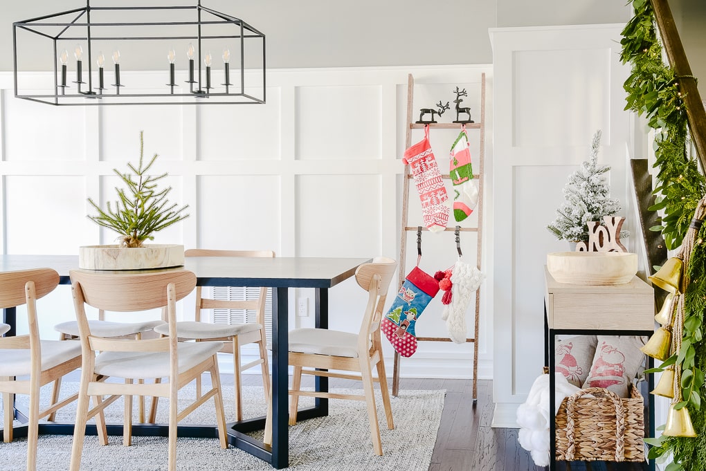 Dining room decorated and styled for Christmas with festive modern decor and staircase greenery garland and stocking ladder