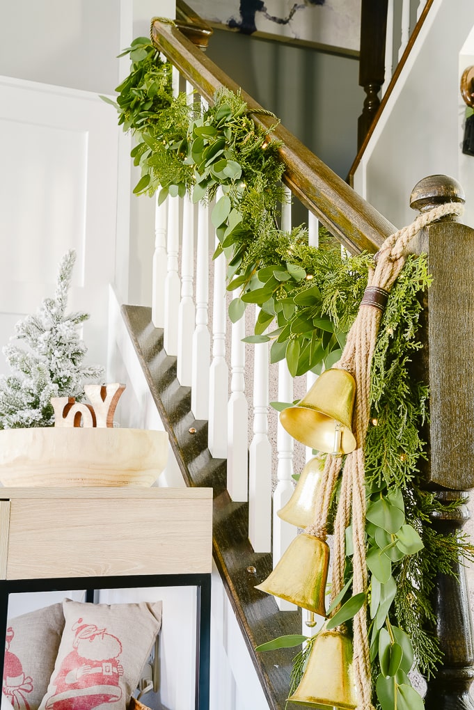 hanging golden Christmas bells attached to pine and eucalyptus Christmas garland on staircase