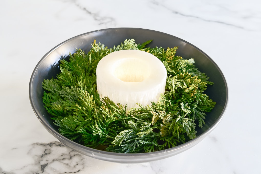 black bowl centerpiece with Christmas greenery and white candle holder in the center