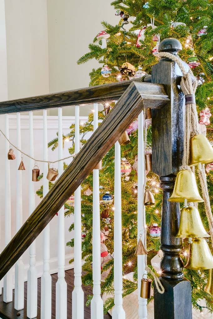 handmade noah bell garland hanging on staircase next to Christmas tree