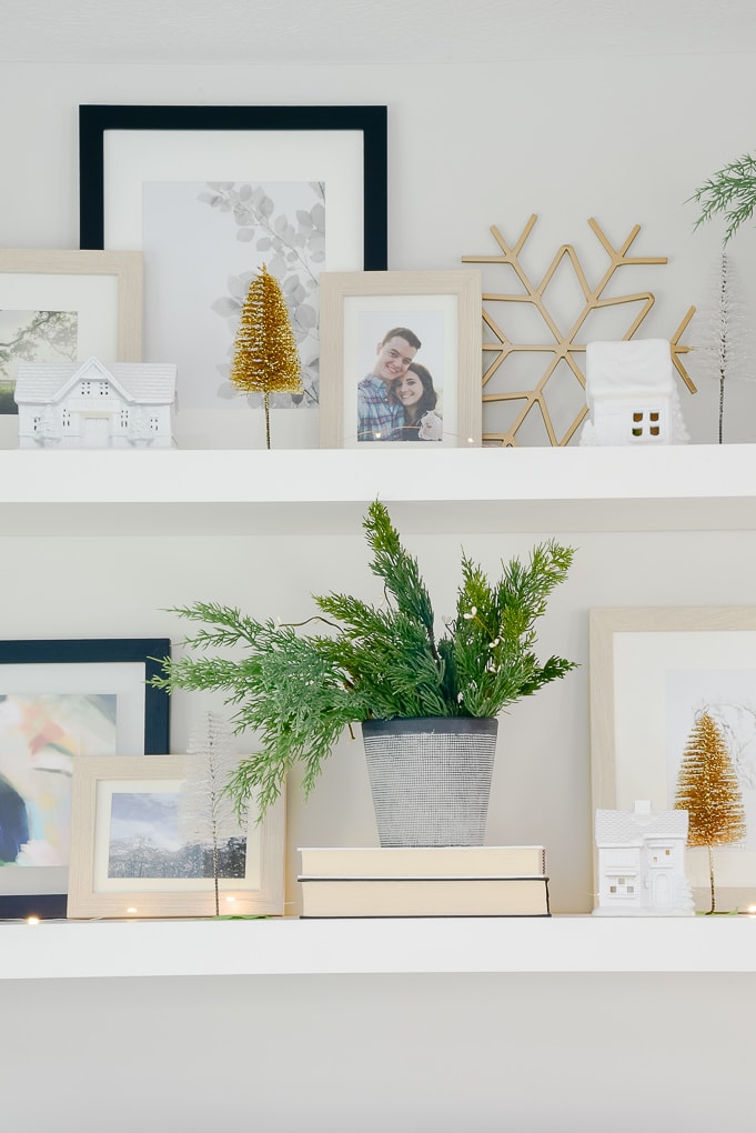 vase of faux Christmas greenery and white Christmas village houses with gold and white bottle brush trees on styled shelves