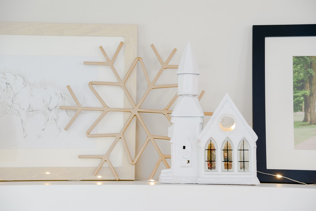 white Christmas village church and gold metal snowflake figurine on styled shelves