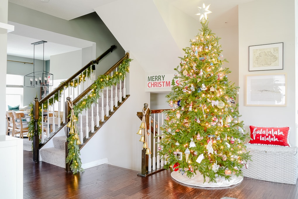 fresh Christmas tree decorated in modern classic living room with family ornaments and greenery garland on staircase