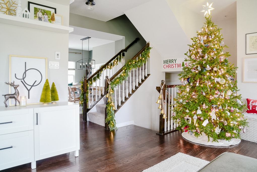 modern classic living room decorated for Christmas with garland on the staircase and fresh Christmas tree in the corner