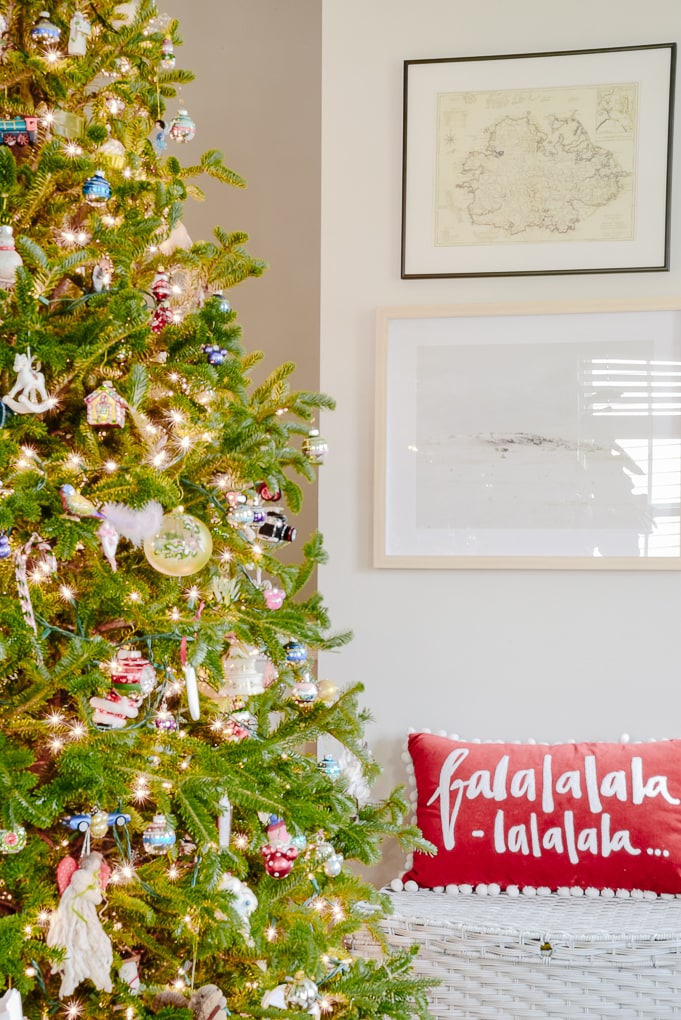 fresh Christmas tree decorated with family ornaments in front of modern artwork on the wall and a Christmas pillow