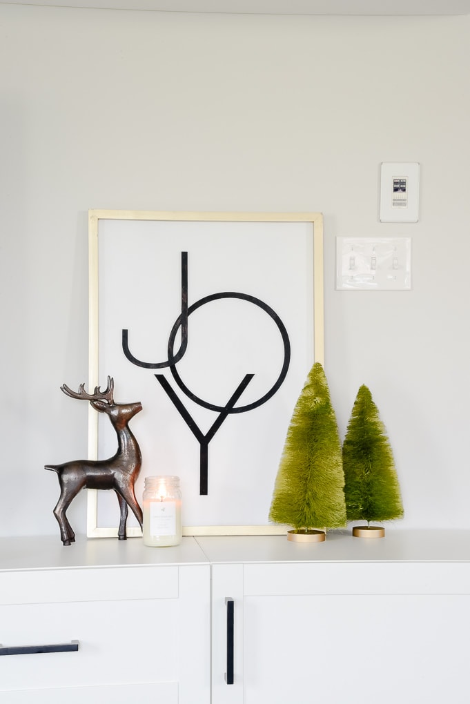 Modern Joy Christmas sign on media center with reindeer figurine and green bottle brush trees and candle