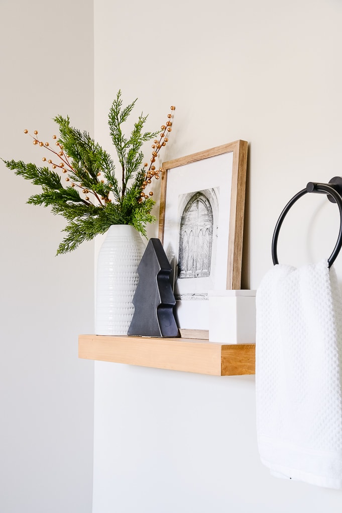 wooden shelf in master bathroom with white vase christmas greenery and black modern tree figurine