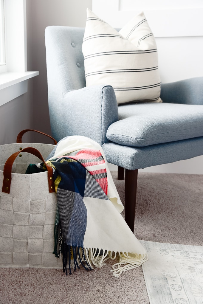 plaid tartan christmas throw blanket inside of a felt basket next to a blue accent chair