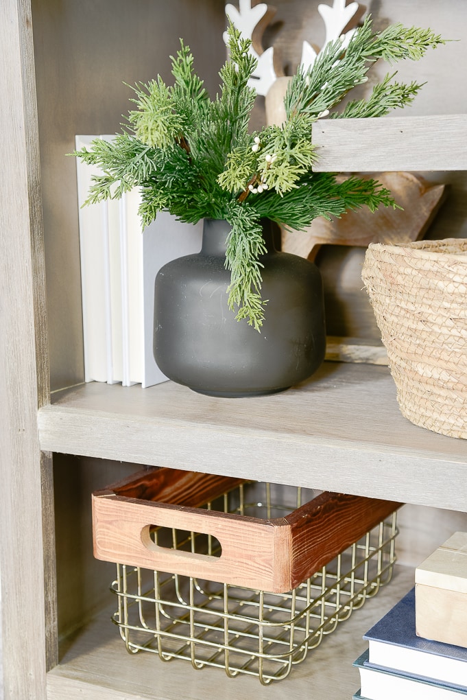 short black vase on bookshelf with faux christmas greenery