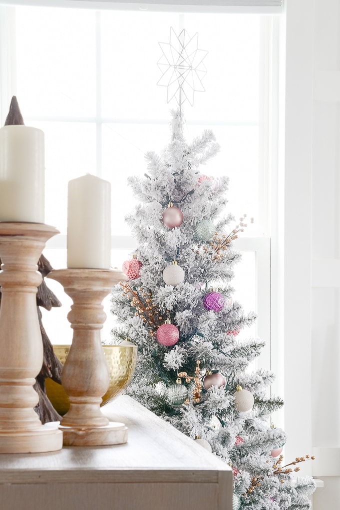 natural wooden pillar candle holders on bookshelf with flocked decorated christmas tree in the background