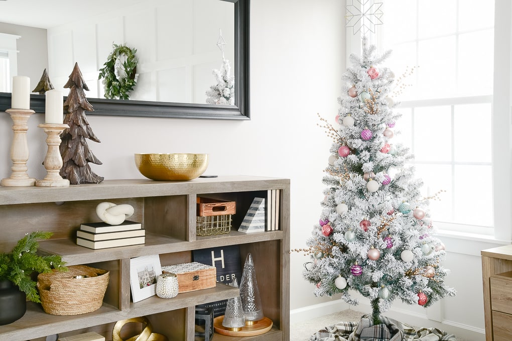 flocked decorated christmas tree next to styled gray bookshelf in master bedroom