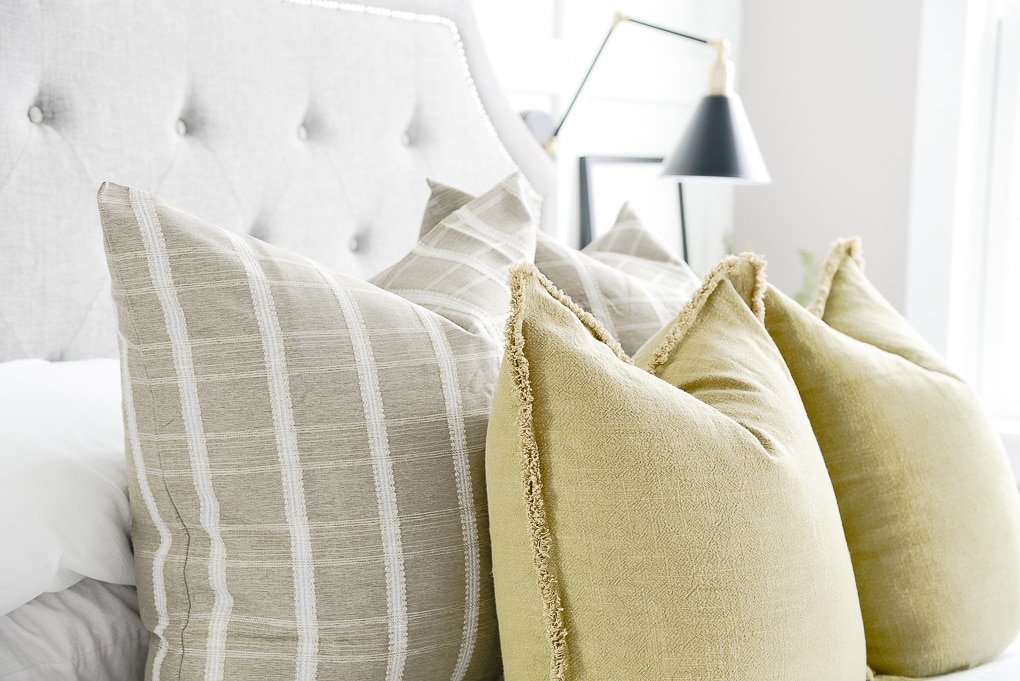 close up of olive throw pillows layered with green windowpane pattern throw pillows on bed in master bedroom