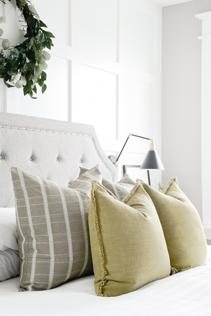 olive throw pillows layered with green windowpane pattern throw pillows on bed in master bedroom with eucalyptus wreath above the bed