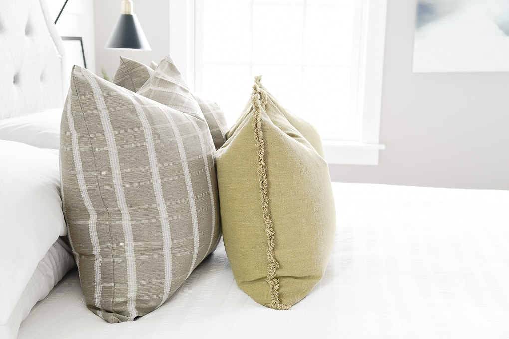 olive throw pillows layered with green windowpane pattern throw pillows on bed in master bedroom