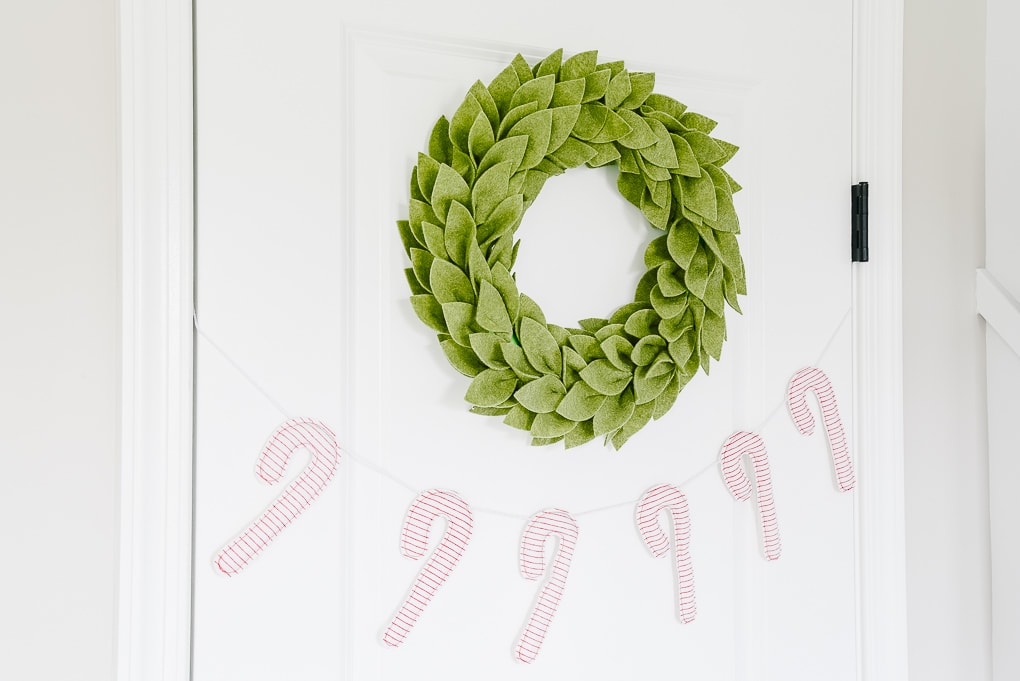 felt greenery wreath on a door above a candy cane christmas garland