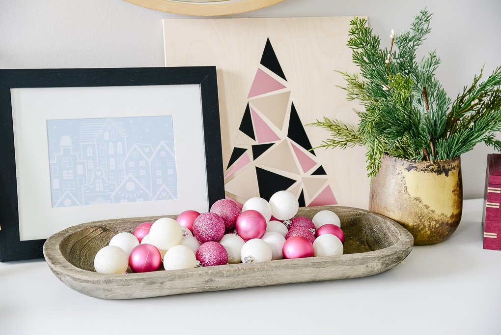 pink and white ornaments in gray tray with christmas artwork behind it