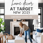 A woman arranges items on a white ottoman in a stylishly decorated living room with white furniture, dark walls, and large windows. A banner above reads: "The Best Studio McGee Home Decor at Target New 2023." The bottom text reads: "christeneholderhome.com.