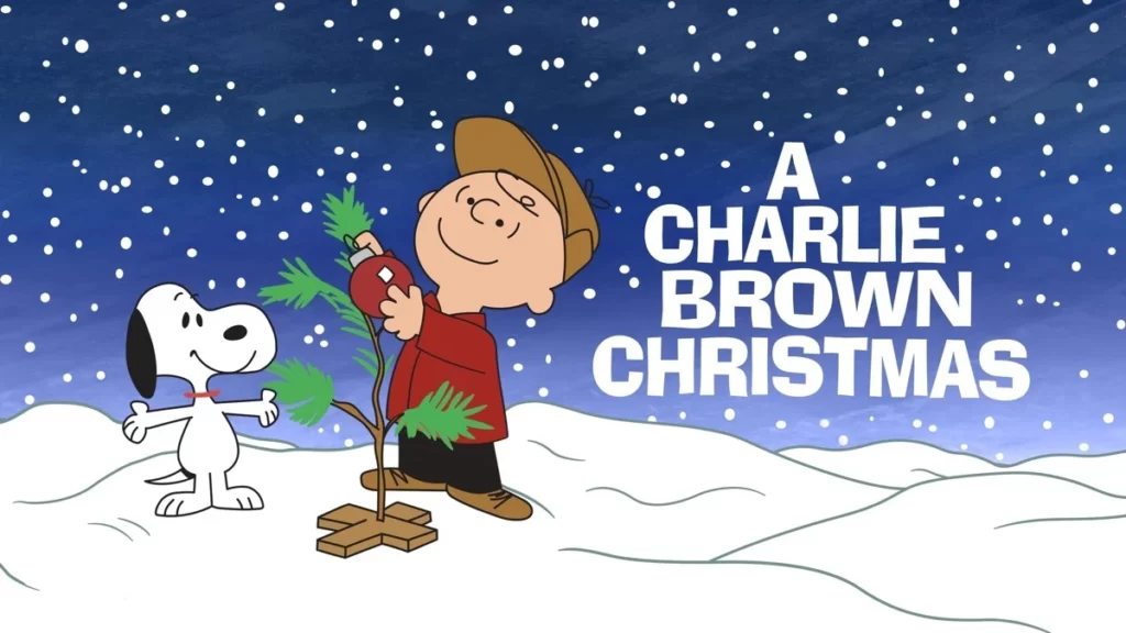 Charlie Brown stands in the snow, decorating a small, sparse Christmas tree with a red ornament. Snoopy, his dog, watches nearby. The text "A Charlie Brown Christmas" is on the right side against a dark blue, starry sky background—a timeless classic and one of the Best Christmas Movies for 4 Year Olds.