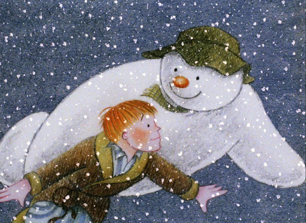 A boy with red hair and a brown coat is seen flying in the air, holding the hand of a large, friendly snowman wearing a green hat. Snow is falling softly around them, creating a whimsical winter scene reminiscent of the best Christmas movies for 4 year olds.