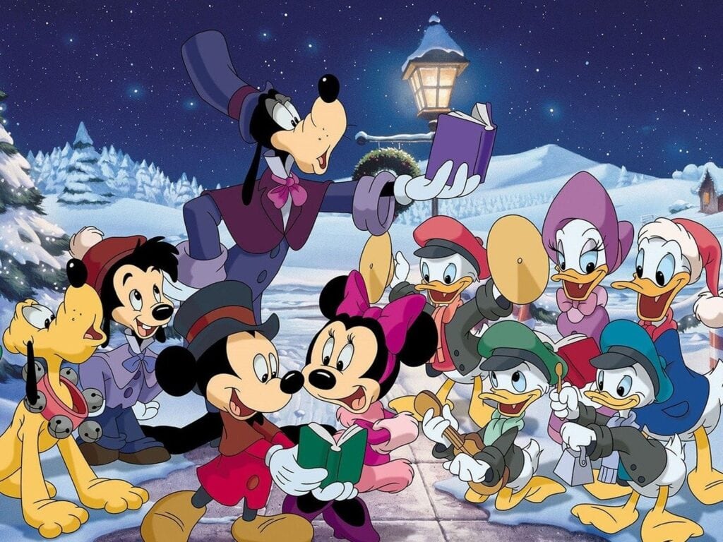 The image shows a snowy nighttime scene featuring Disney characters Mickey Mouse, Minnie Mouse, Donald Duck, Daisy Duck, Goofy, Pluto, and Huey, Dewey, and Louie. All dressed warmly in winter clothes and caroling together, it's reminiscent of the best Christmas movies for 4-year-olds.