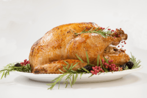 A roasted chicken on a white platter, garnished with rosemary, red berries, and blackberries, offers a delightful centerpiece for Thanksgiving meal planning—a perfect time-saving tip for busy moms aiming to impress without the stress.