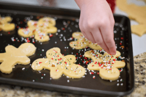 A hand decorates gingerbread-shaped cookies with colorful sprinkles on a granite surface, capturing a festive baking moment. As you prepare for baking, remember that organizing your pantry for Christmas ensures everything is ready for these joyous creations.